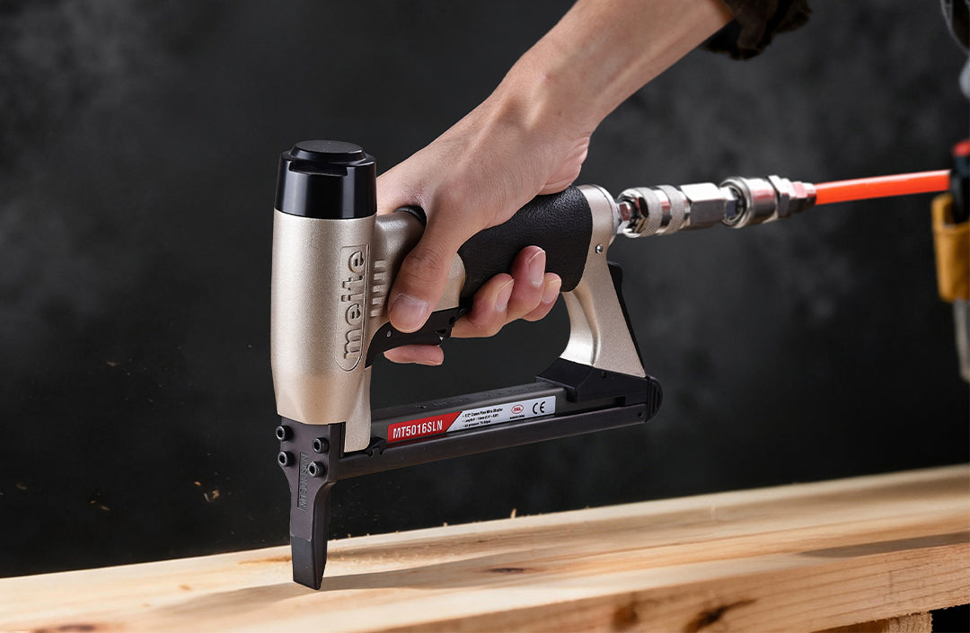 Meite USA MT5016SLN 20 gauge pneumatic stapler driving staples into a wooden board with a dark background.